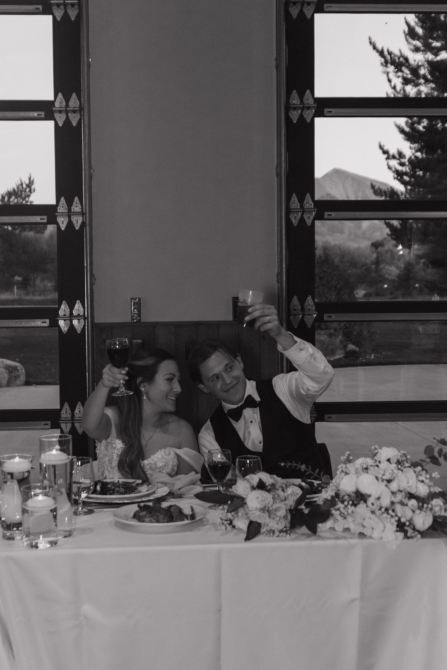 Black and white photo of a couple toasting at their wedding reception table.