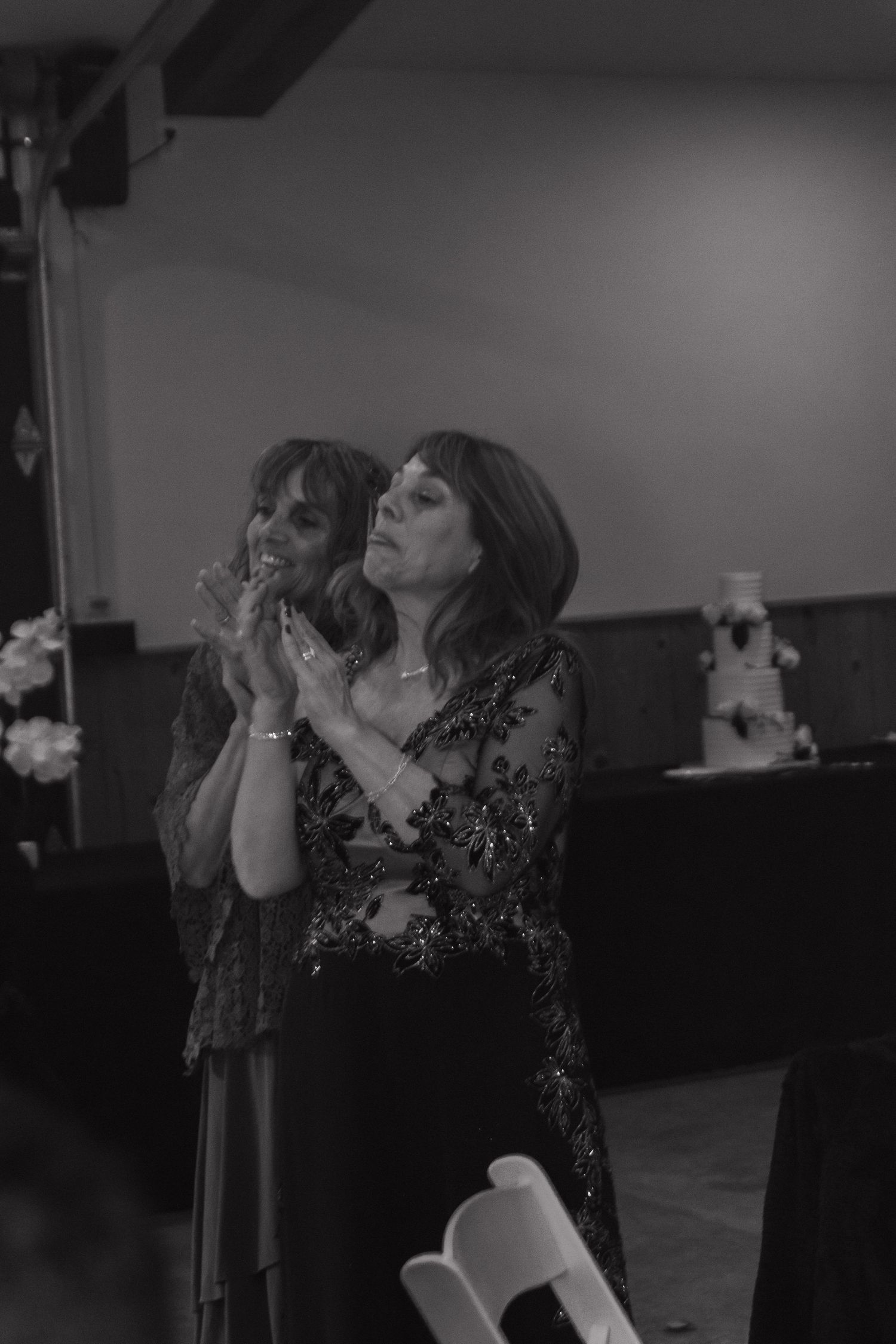 Two guests in formal attire share an emotional moment during a celebration in a dimly lit reception hall.