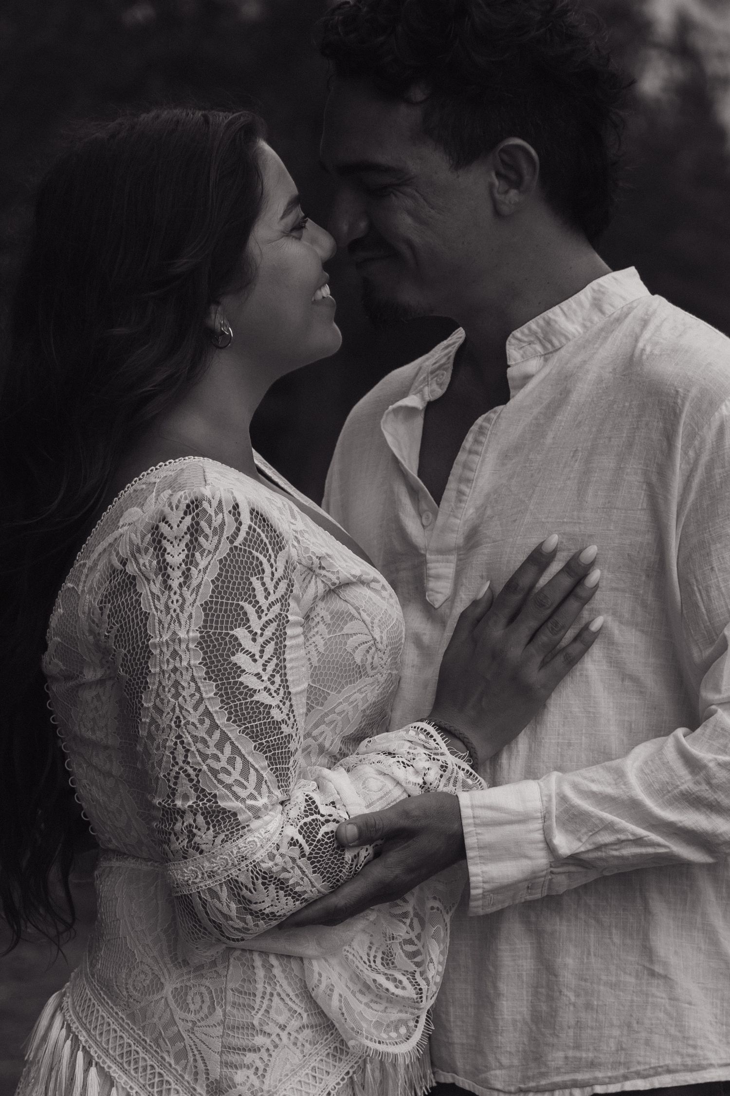 Black and white photo of a romantic couple in elegant attire sharing an intimate moment outdoors.
