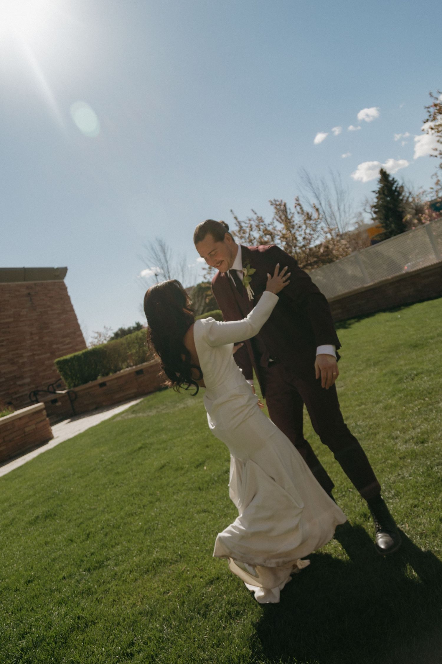 Bride and groom dancing on green lawn under bright blue sky during outdoor wedding celebration.