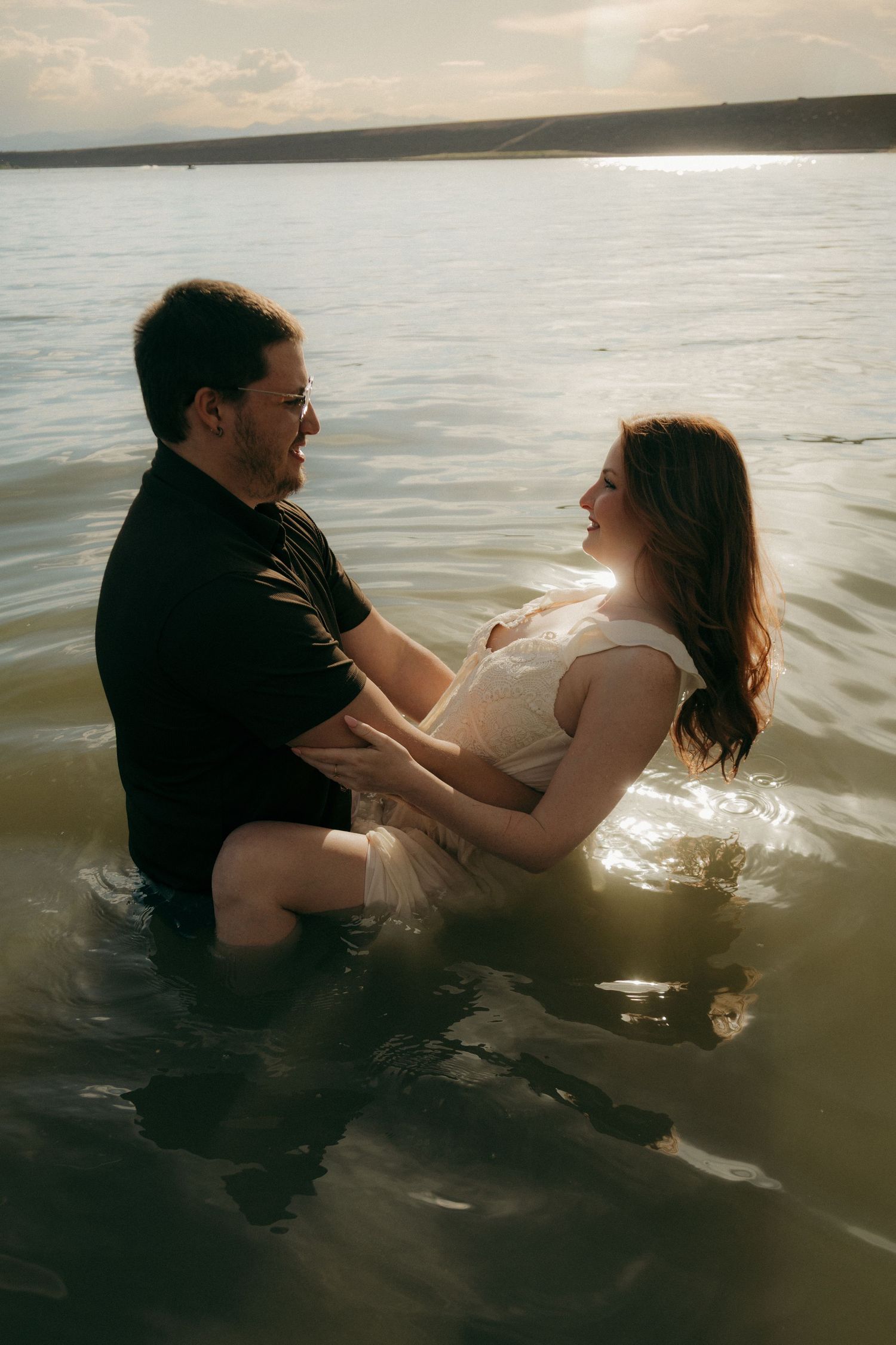 Couple sharing a romantic moment together while standing in a sunlit lake, smiling at each other.
