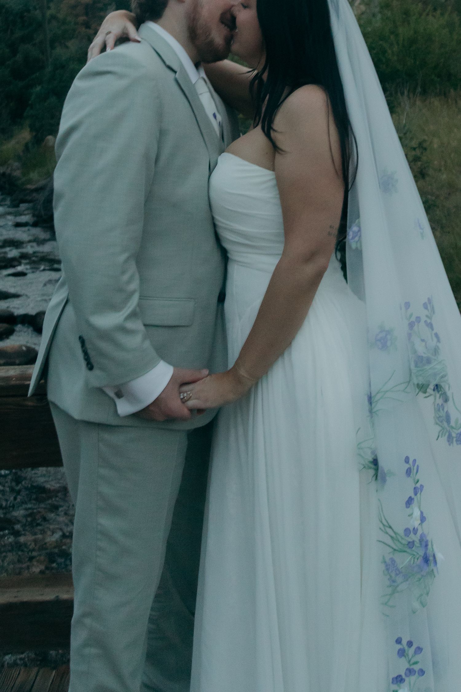 Bride and groom share romantic kiss on wooden bridge, bride in floral veil.