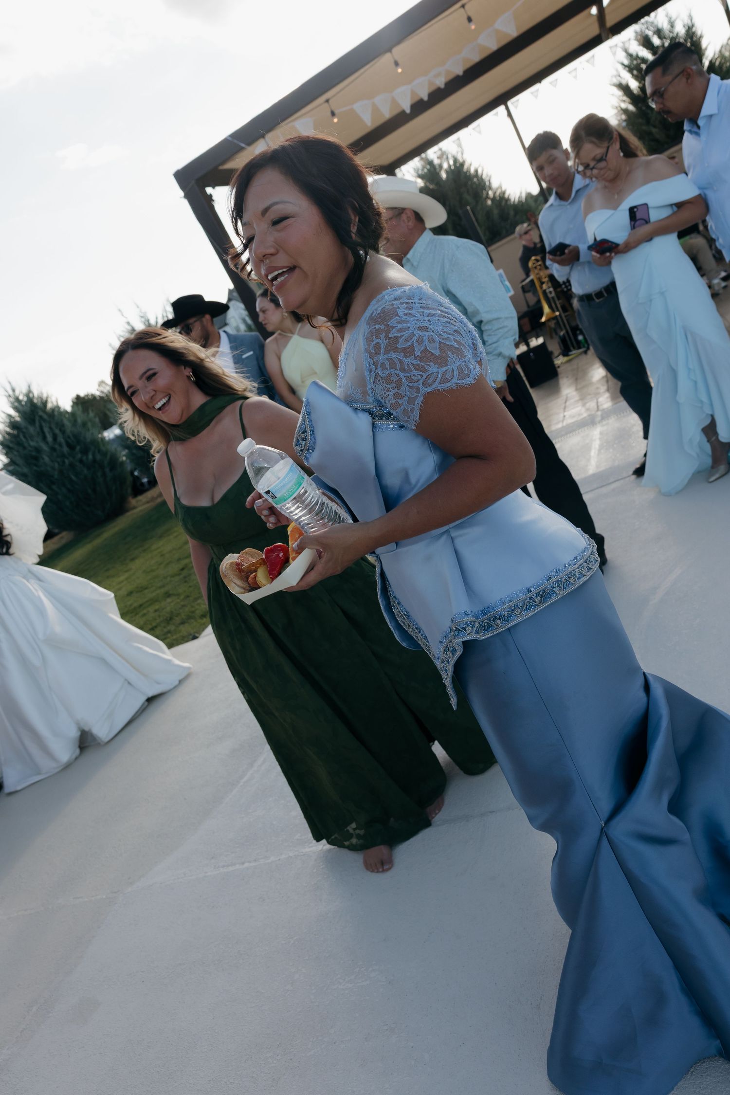 Wedding guests in blue and green dresses laugh and socialize on outdoor dance floor at reception.