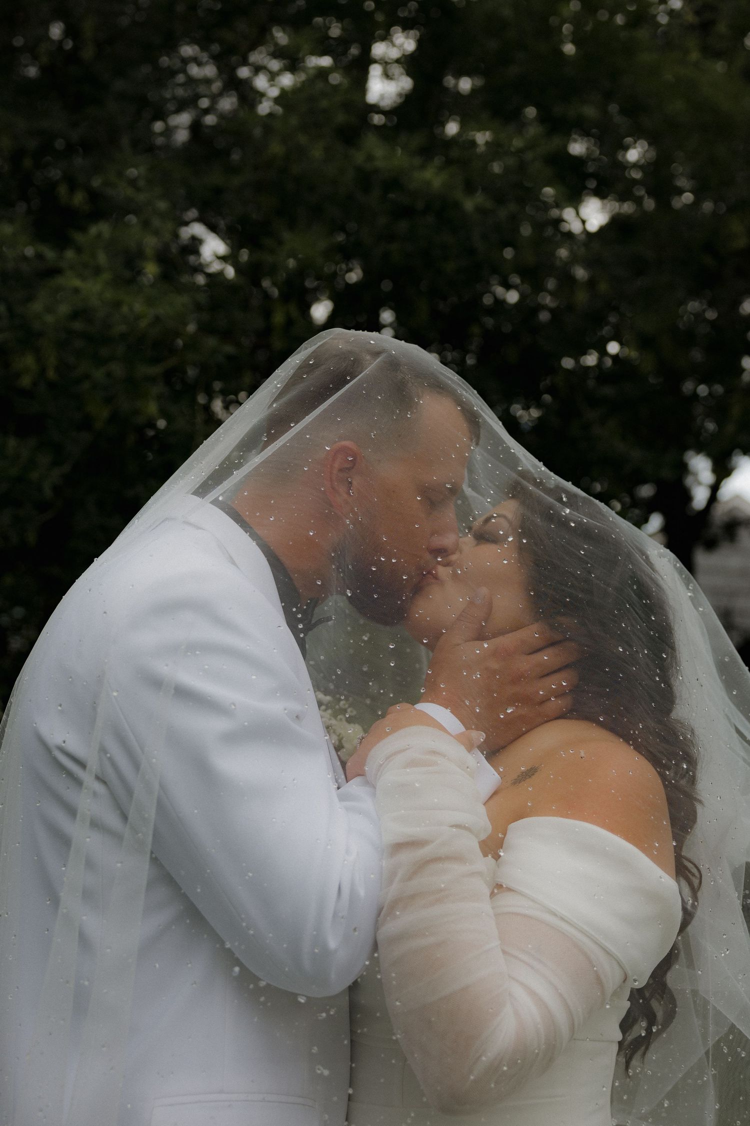 Bride and groom share a romantic kiss under a dotted wedding veil outdoors.