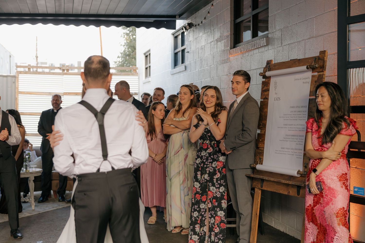 Wedding guests gathering outdoors near menu board at rustic venue cocktail hour.