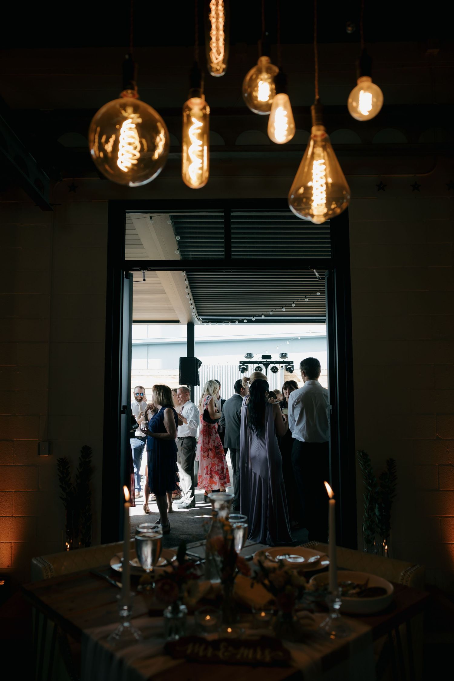 Elegant wedding reception venue with vintage Edison bulb pendant lights illuminating guests gathered in doorway.