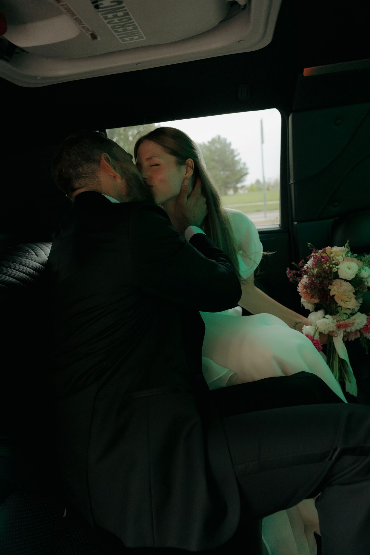 Newlywed couple sharing a romantic kiss in the back of a limousine after their wedding ceremony.