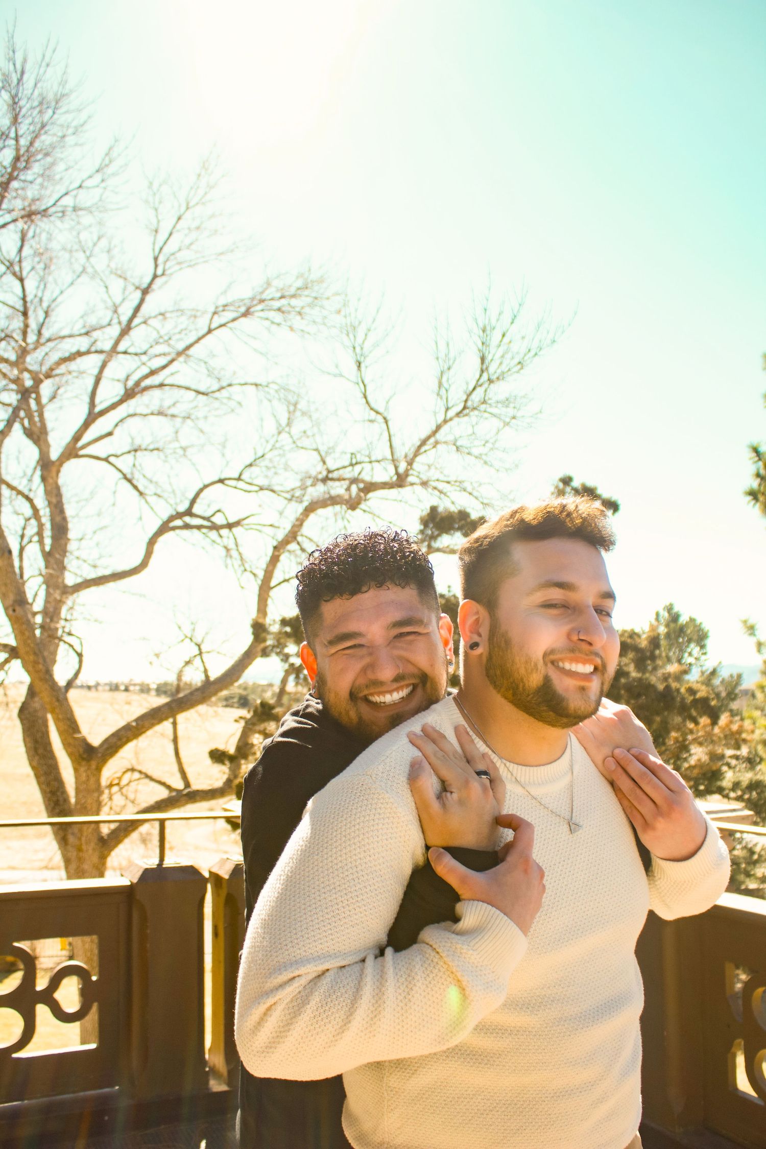 Two people sharing a joyful embrace on a balcony with bare trees in the background.