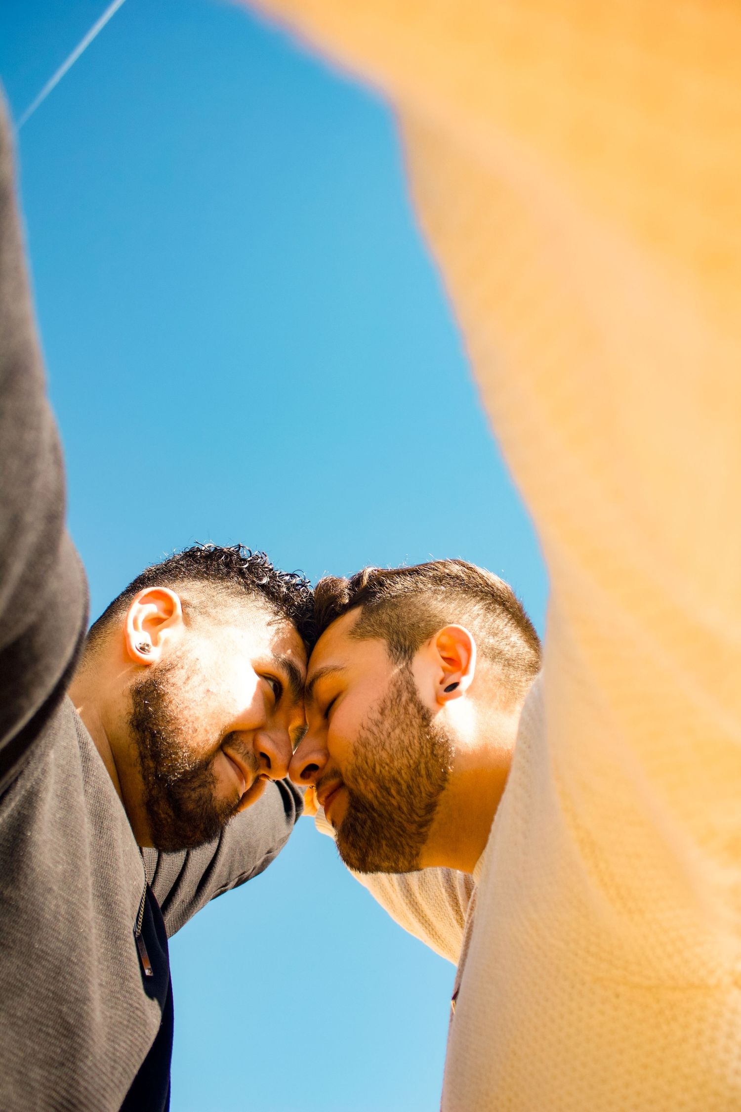 Close-up portrait of two people touching foreheads against blue and orange background.