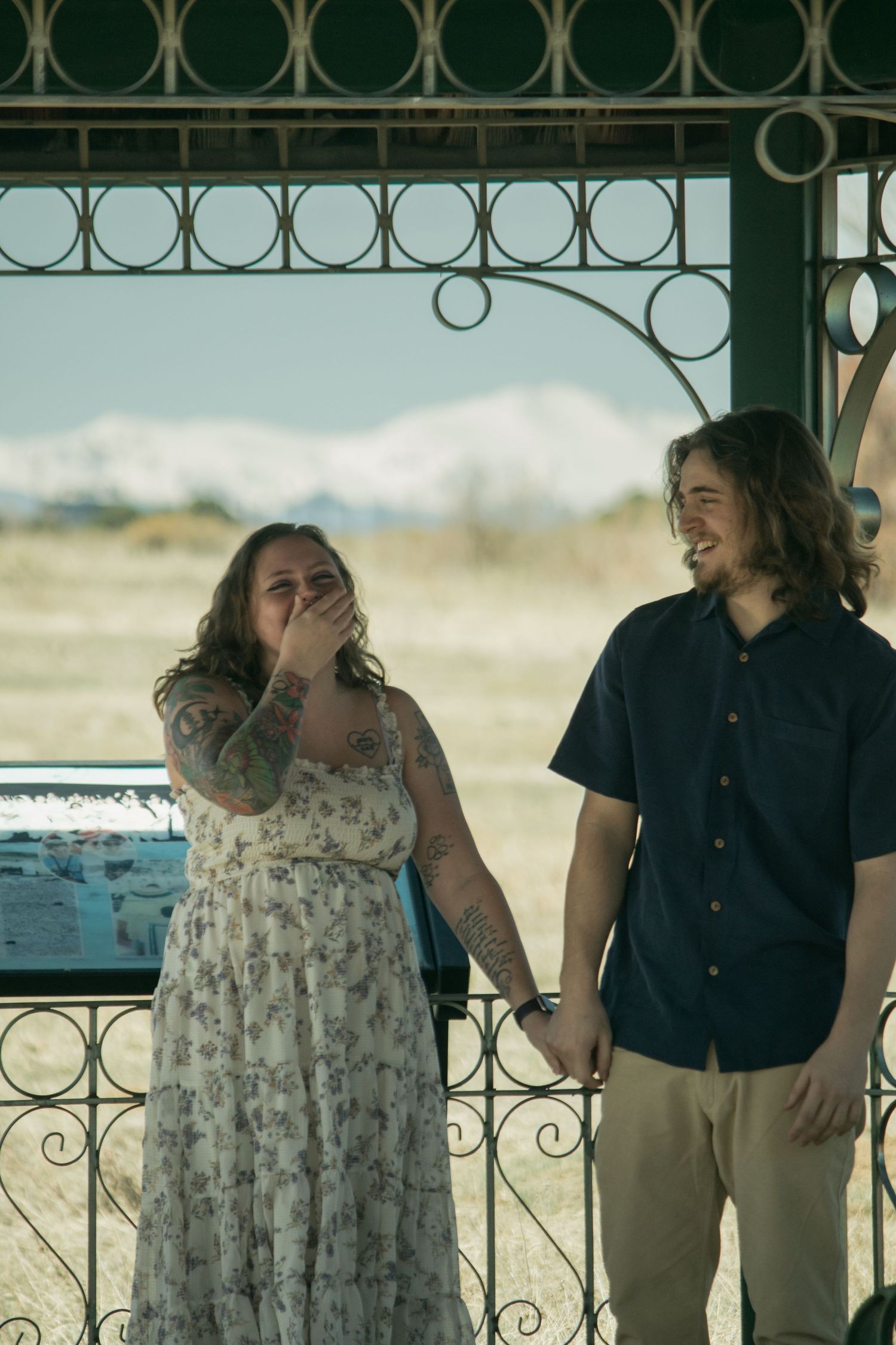 A couple shares a joyful moment together on a porch with decorative iron railings.