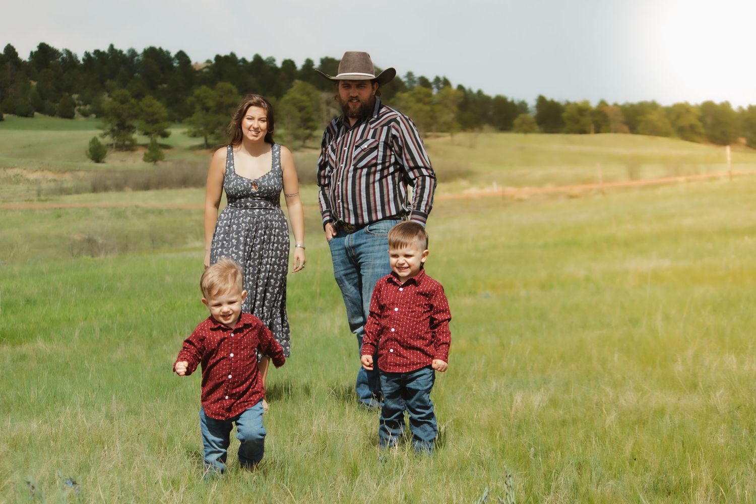 A family walking together through a scenic meadow with pine trees in the background.
