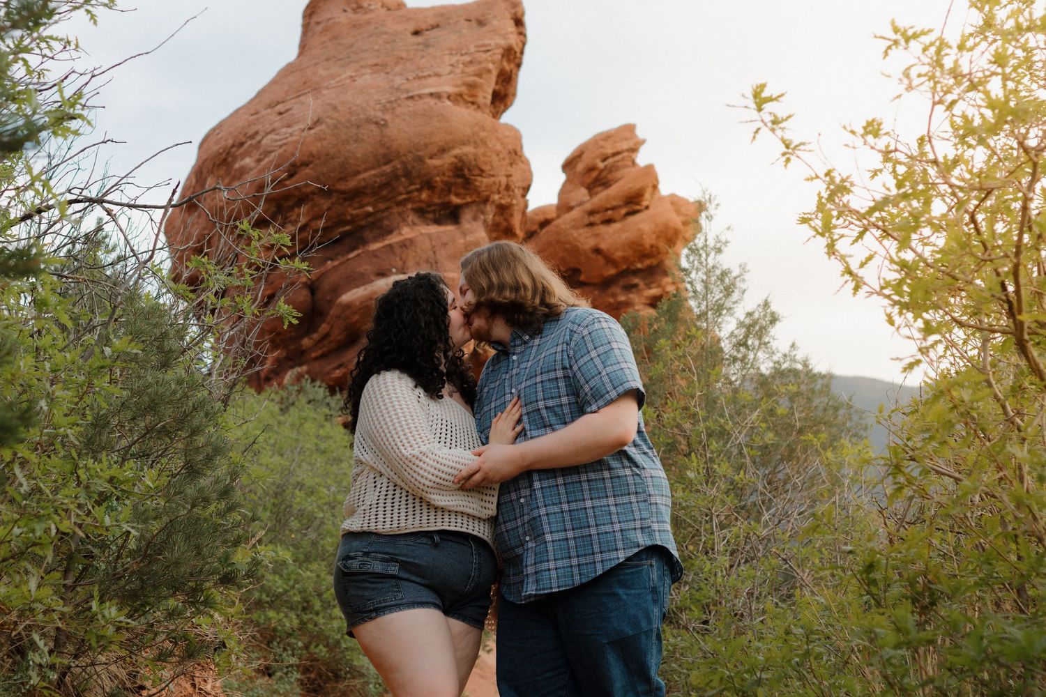 A loving couple embraces in front of scenic red rock formations during golden hour.