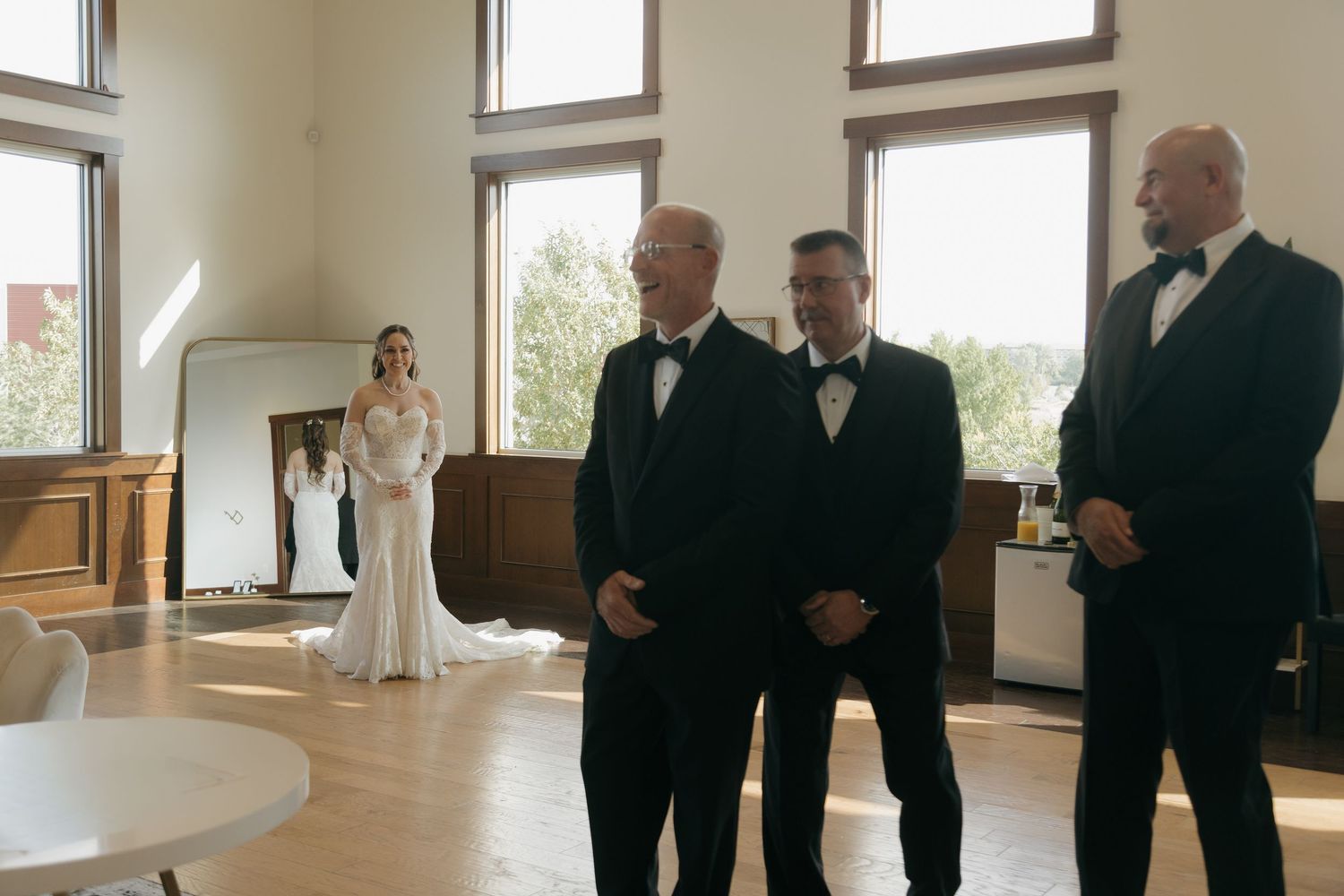Groom and groomsmen in black tuxedos await bride's entrance during wedding first look indoors.