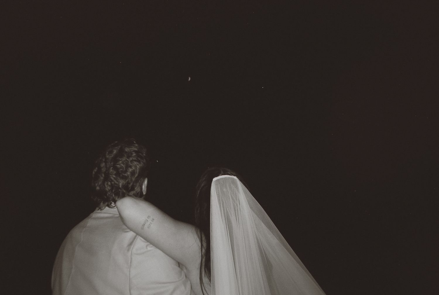 Black and white film photo of bride and groom gazing at the night sky.