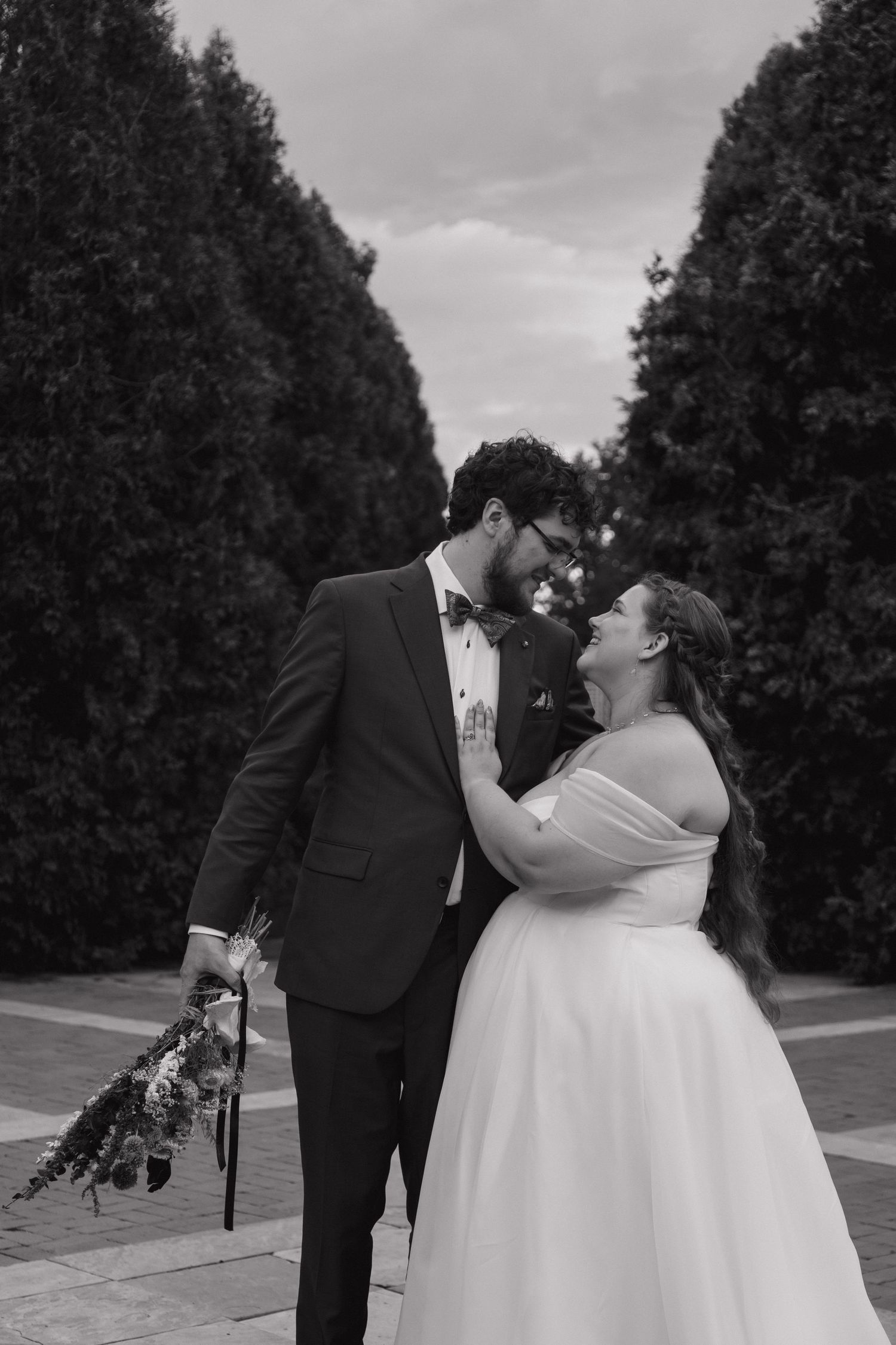 Black and white photo of bride and groom sharing a joyful moment among tall trees.