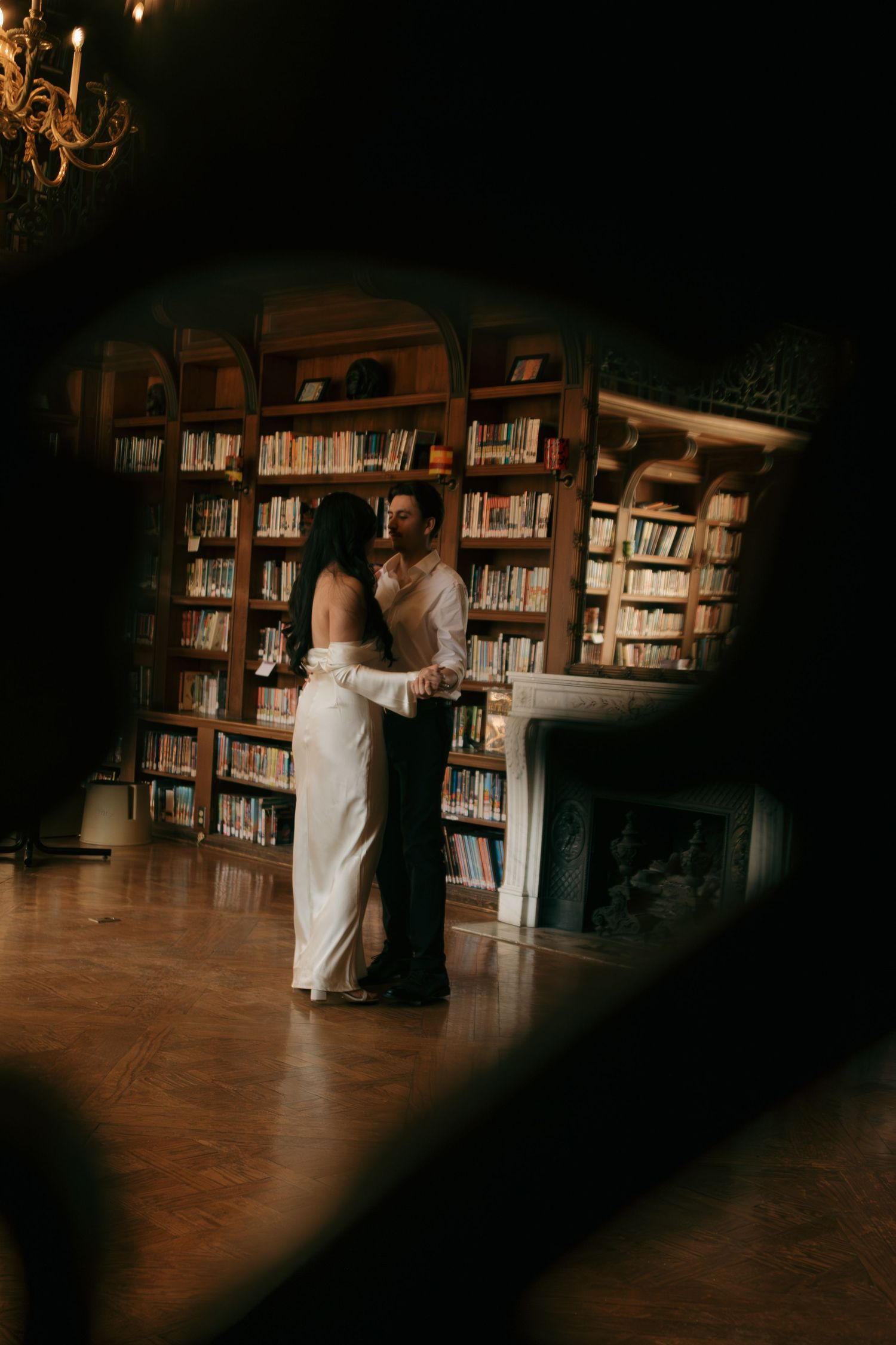 Moody library interior with wooden bookshelves and dramatic shadows cast across hardwood floors.