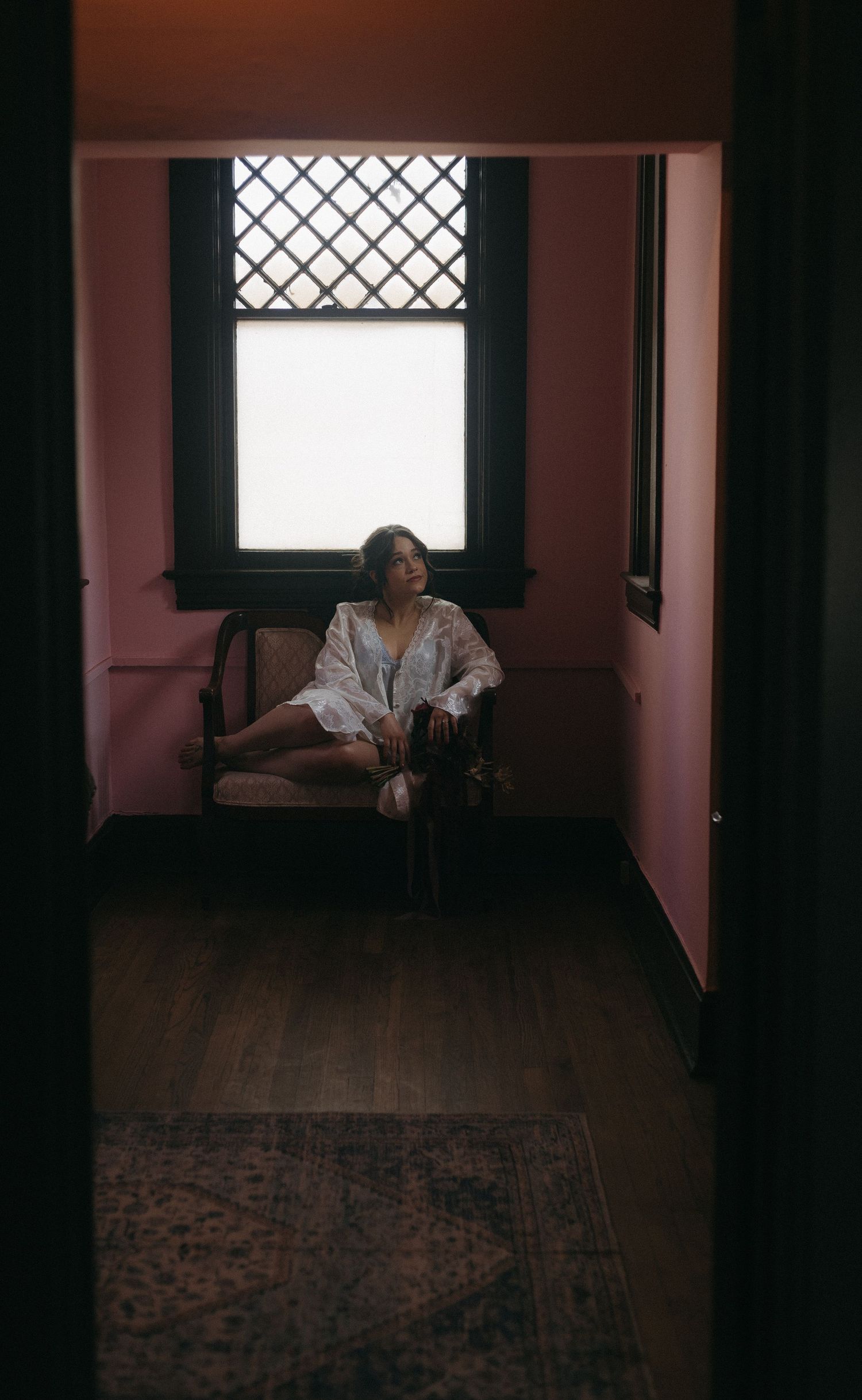 A moody interior scene with pink walls and a window with lattice detail, featuring a white robe in dim lighting.
