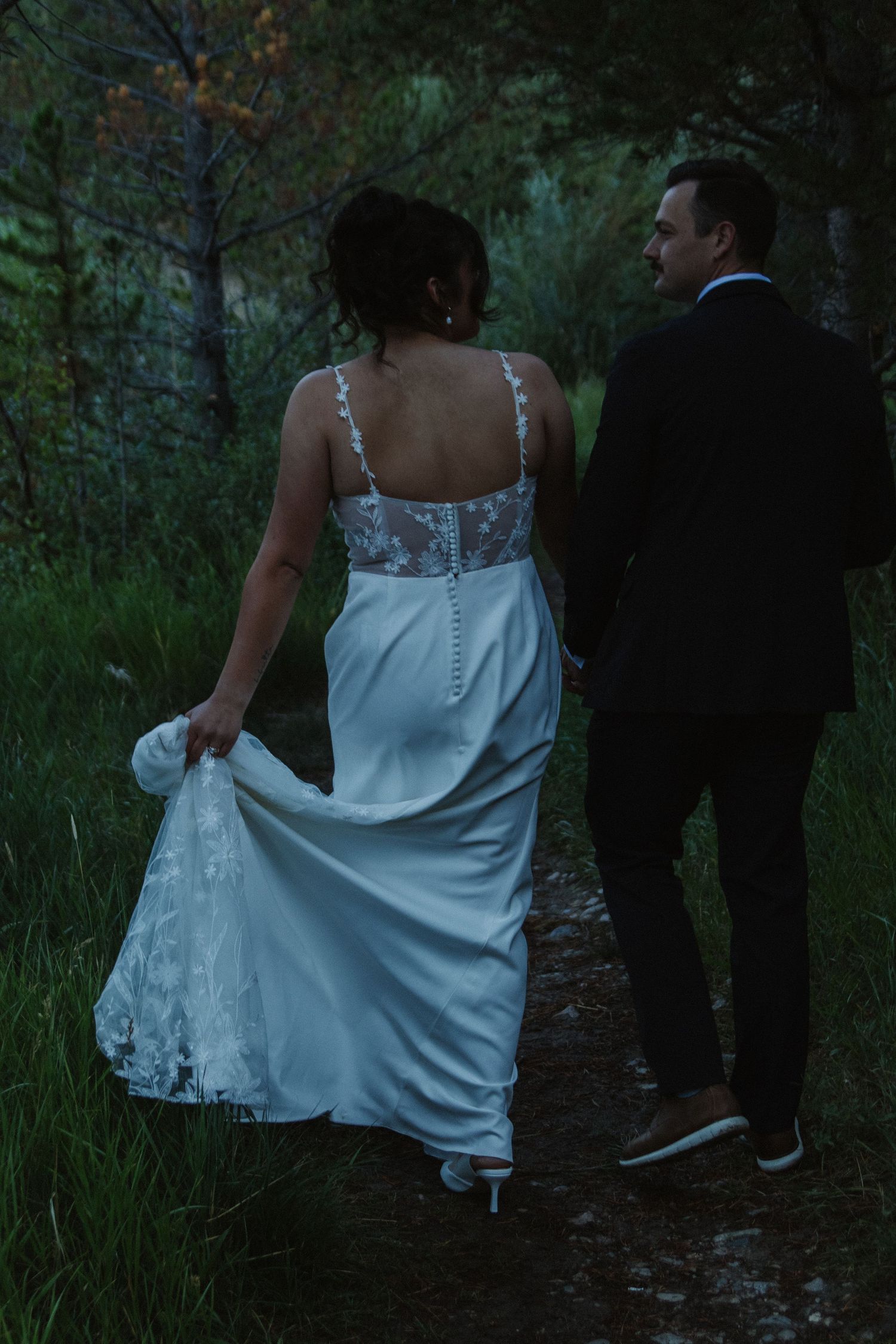 Wedding party walks through mountain trail at dusk near lake.