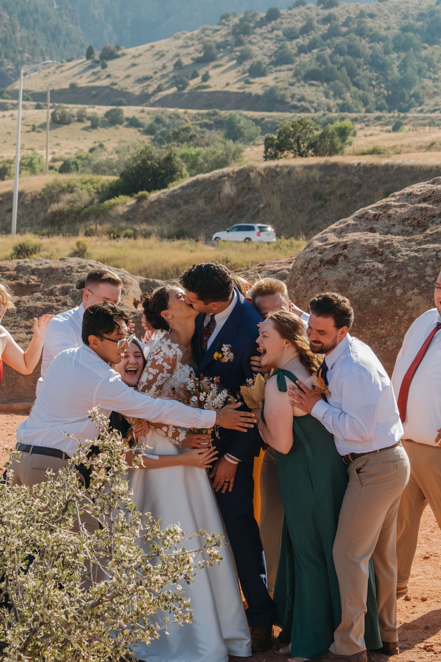 Wedding party celebrates together on rocky terrain with mountains in the background.