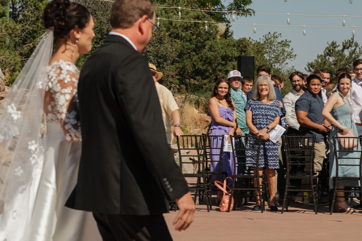 Outdoor wedding ceremony with guests watching couple at rustic wooden pergola venue.