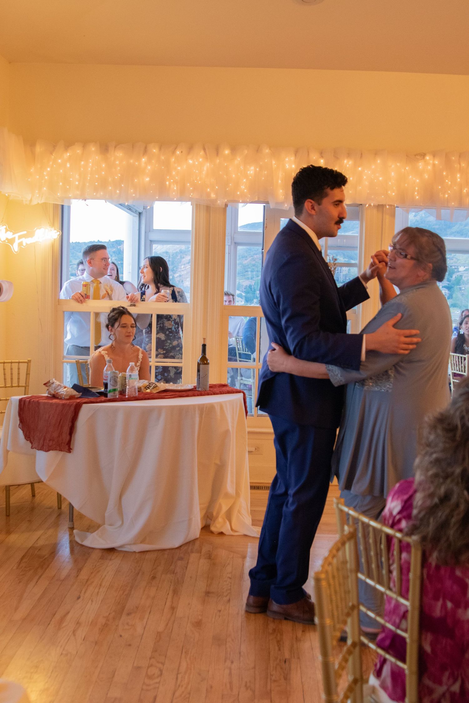 Wedding reception scene with string lights and guests mingling in warm-lit venue.
