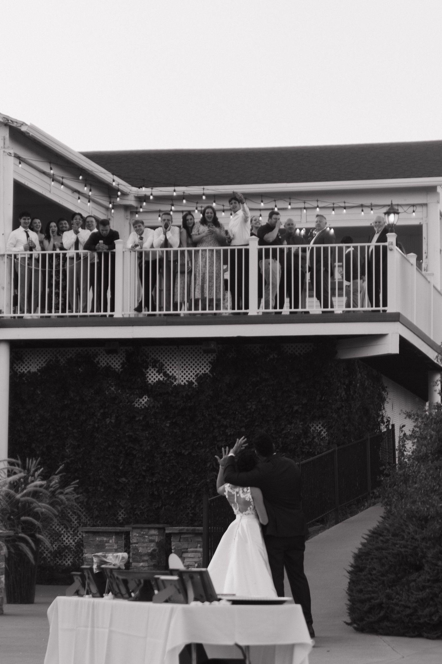 Wedding guests watch from a balcony as the couple celebrates below.