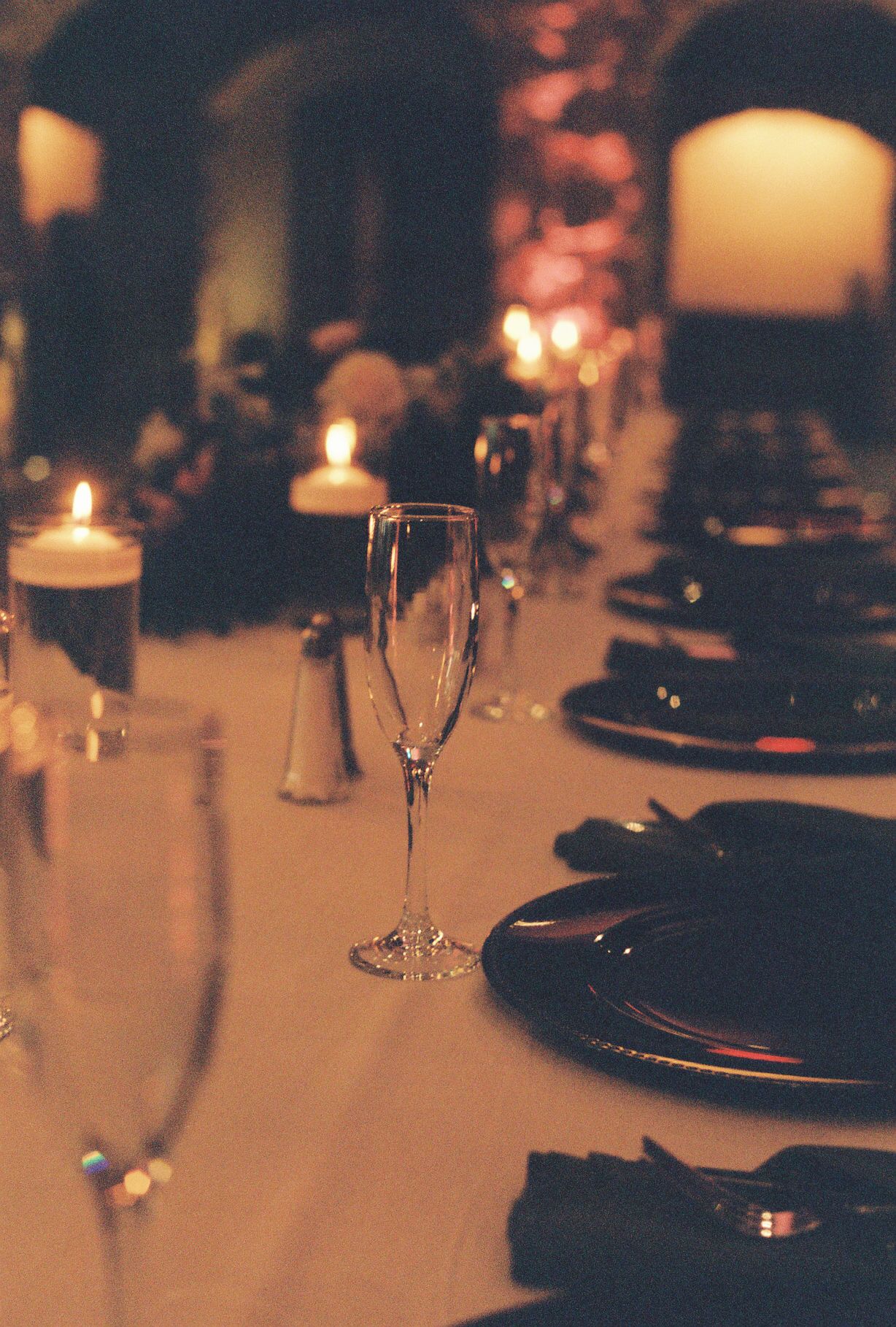 Elegant wedding table setting with champagne flutes, black plates, candles in warm stone venue.