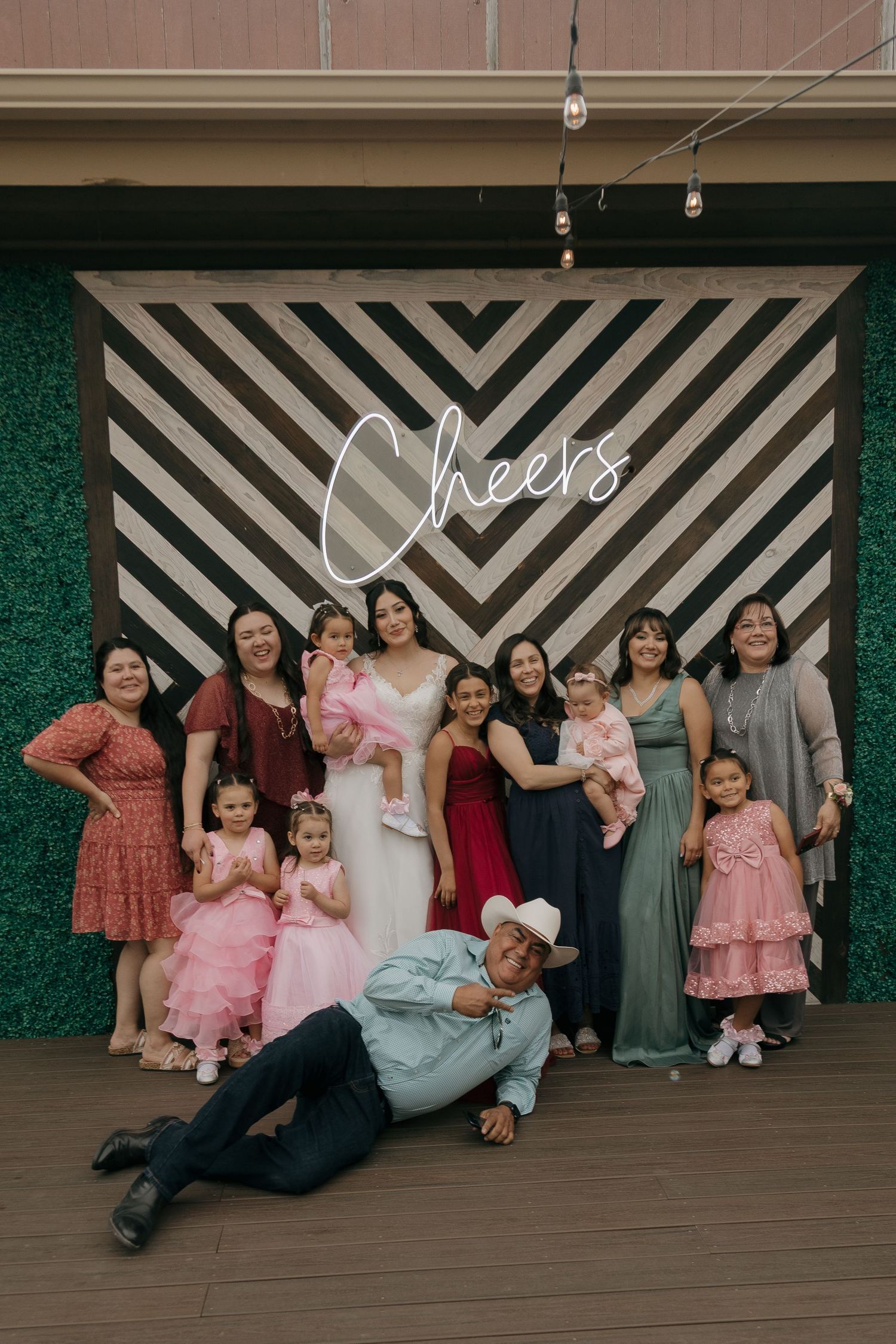 Bride with family and children posing in front of Cheers neon sign on striped chevron backdrop.