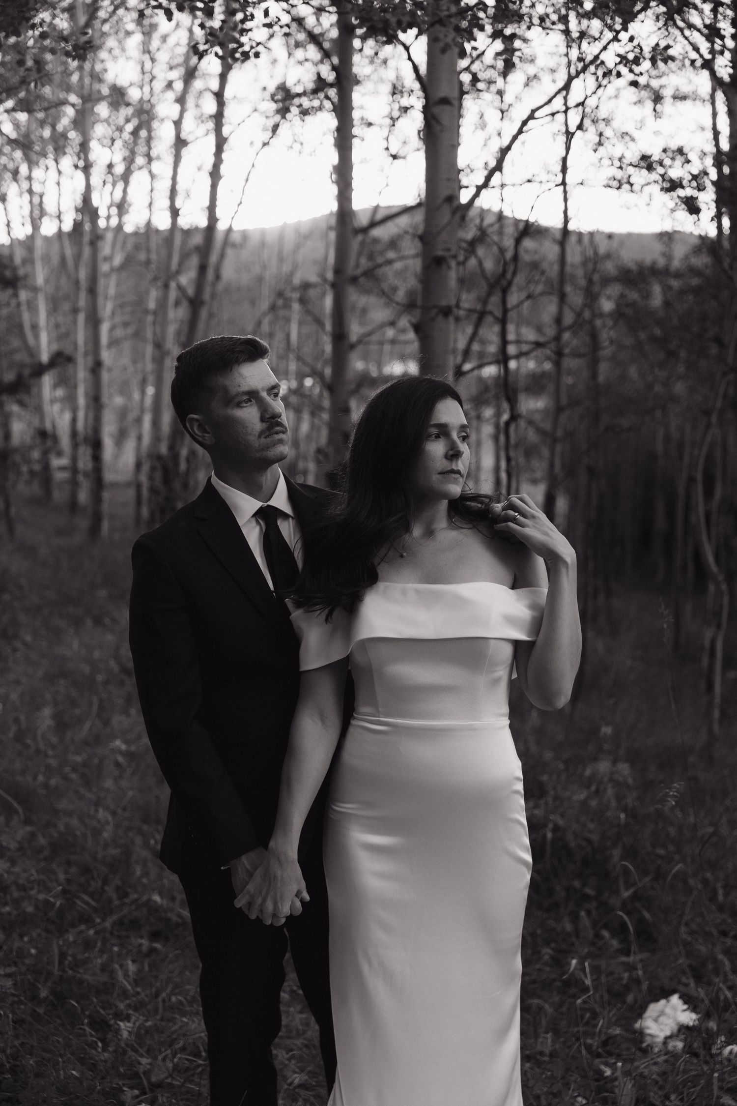 Black and white portrait of bride and groom standing together in a birch forest with a moody, elegant atmosphere.