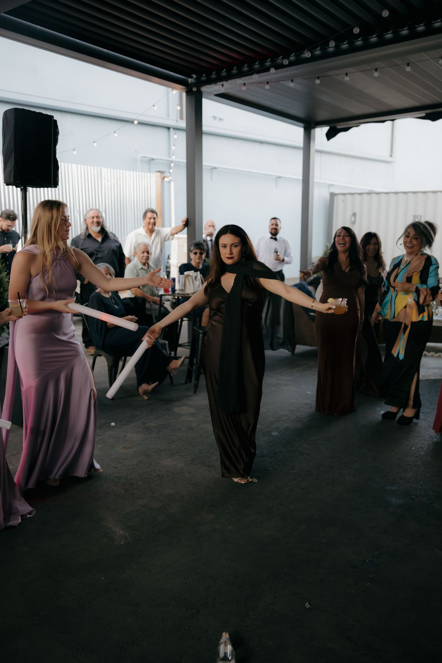 Woman in black dress performs a candle ceremony walk at an outdoor wedding reception celebration.