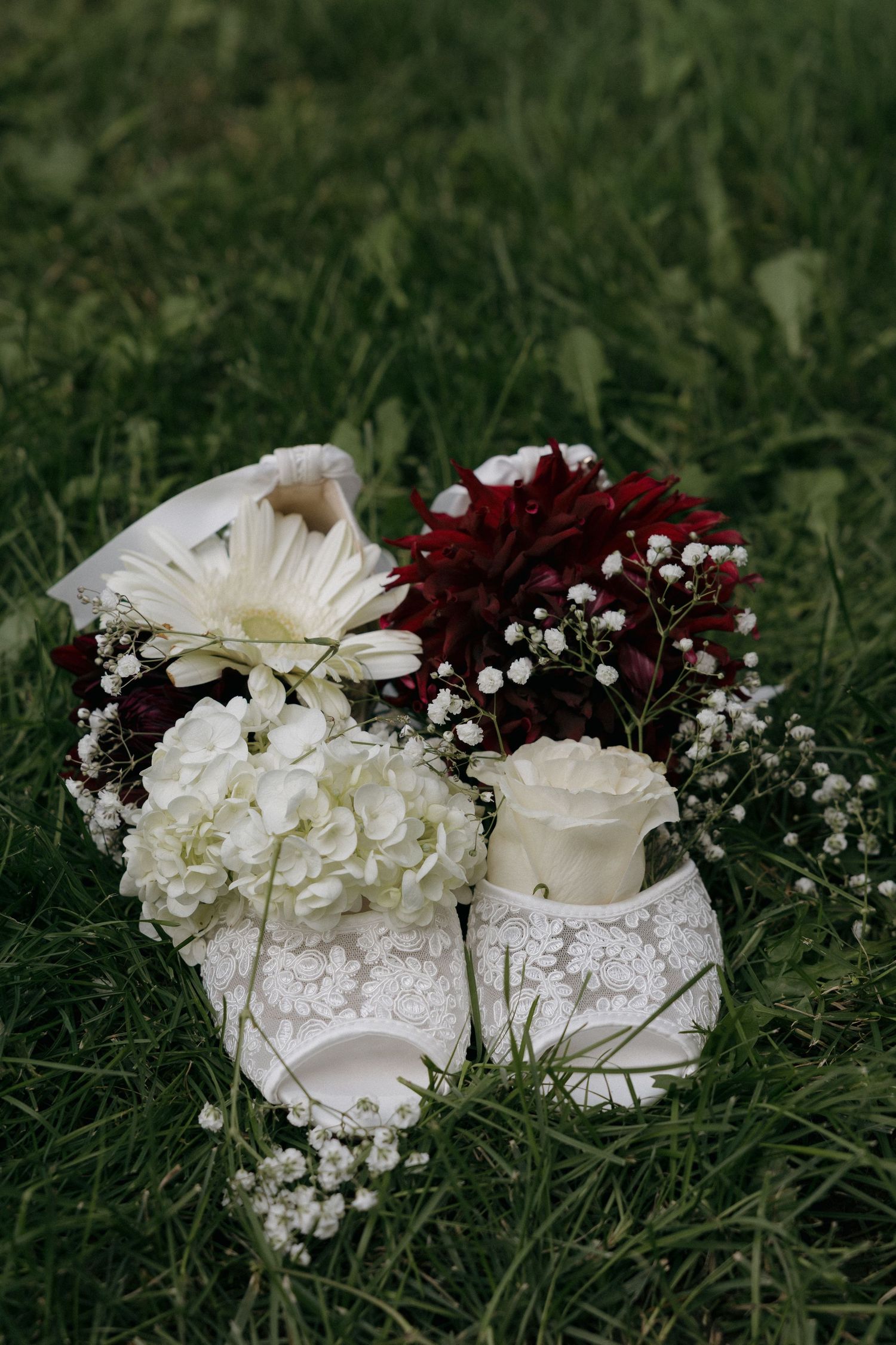 Bridal white lace shoes surrounded by red and white wedding flowers on green grass.