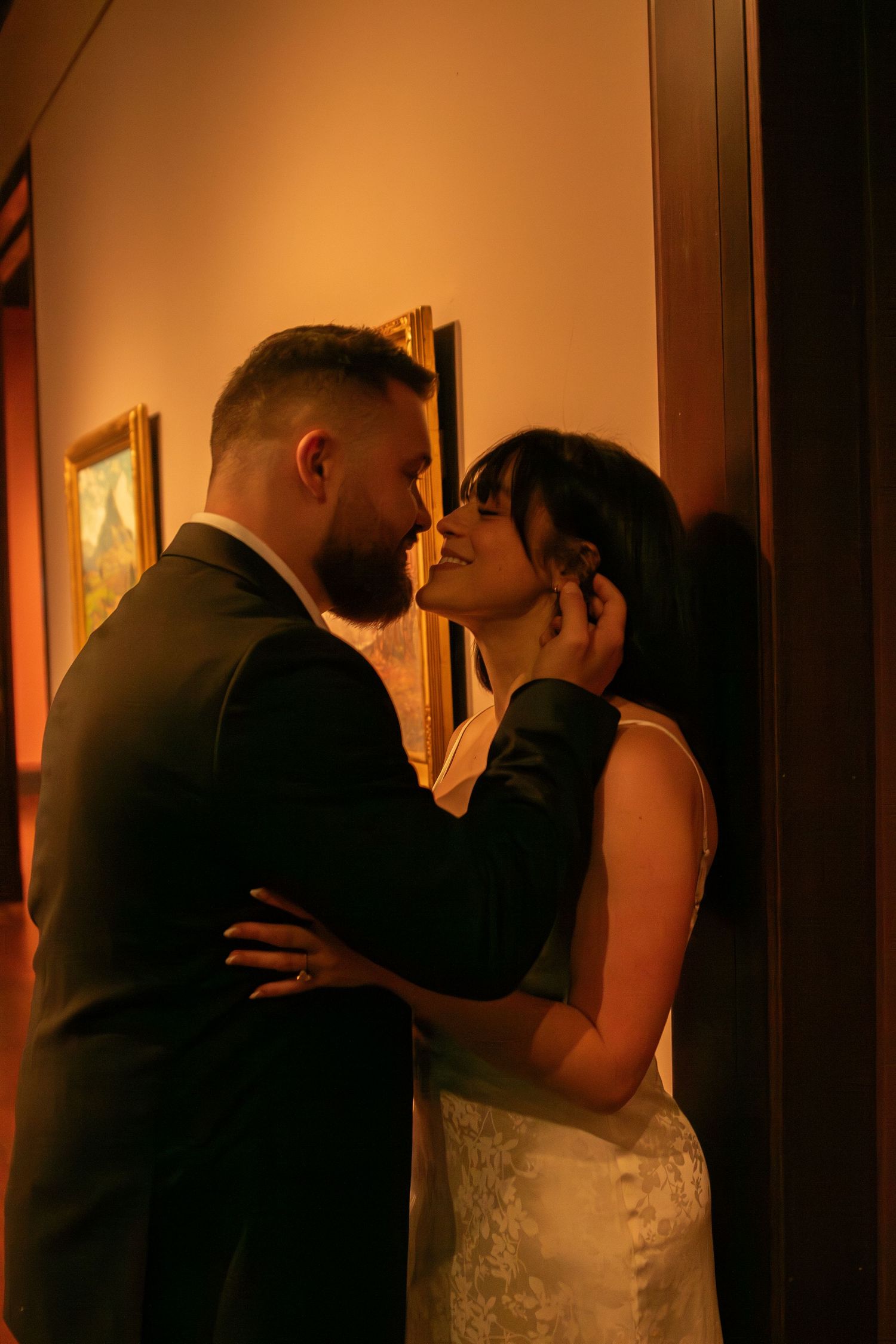 Intimate couple embracing in warm lighting against dark hallway backdrop.
