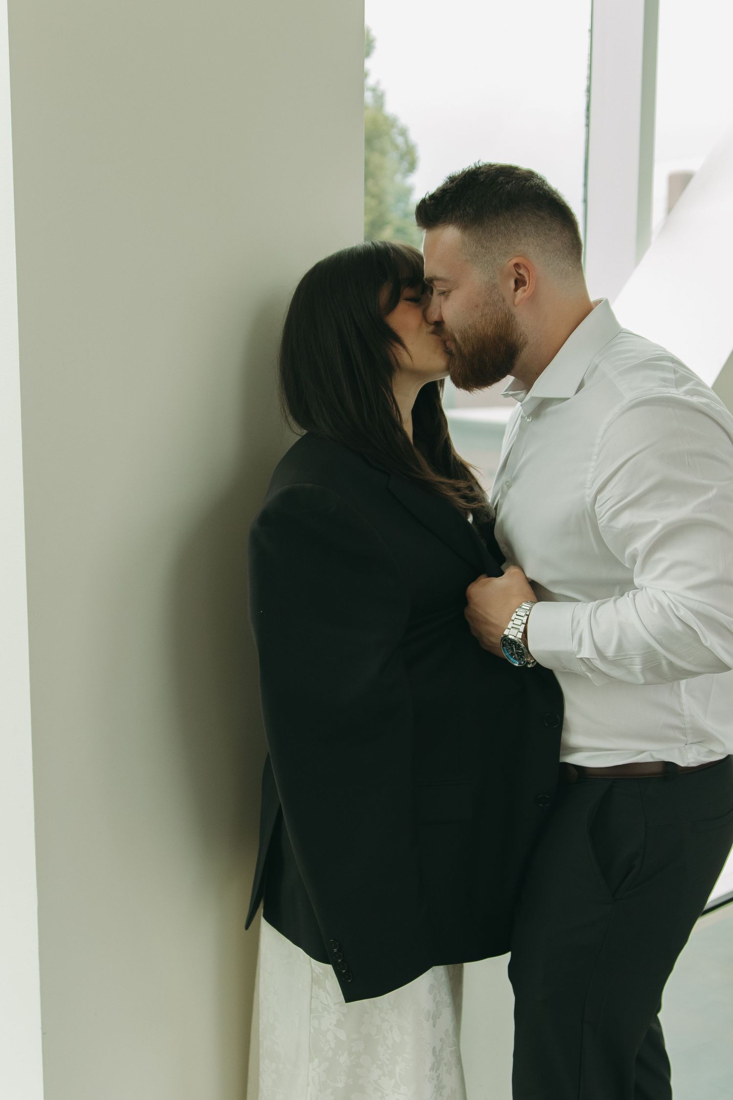 A couple shares an intimate moment against a stark white wall.