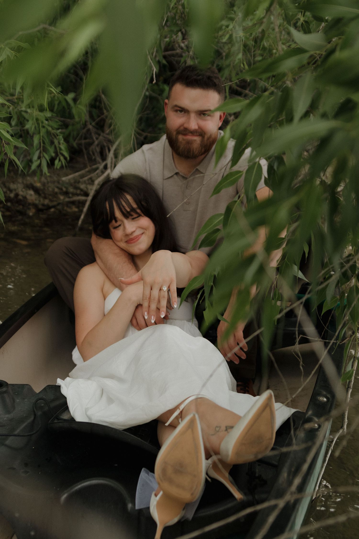 A couple poses under green foliage during a romantic outdoor photoshoot.