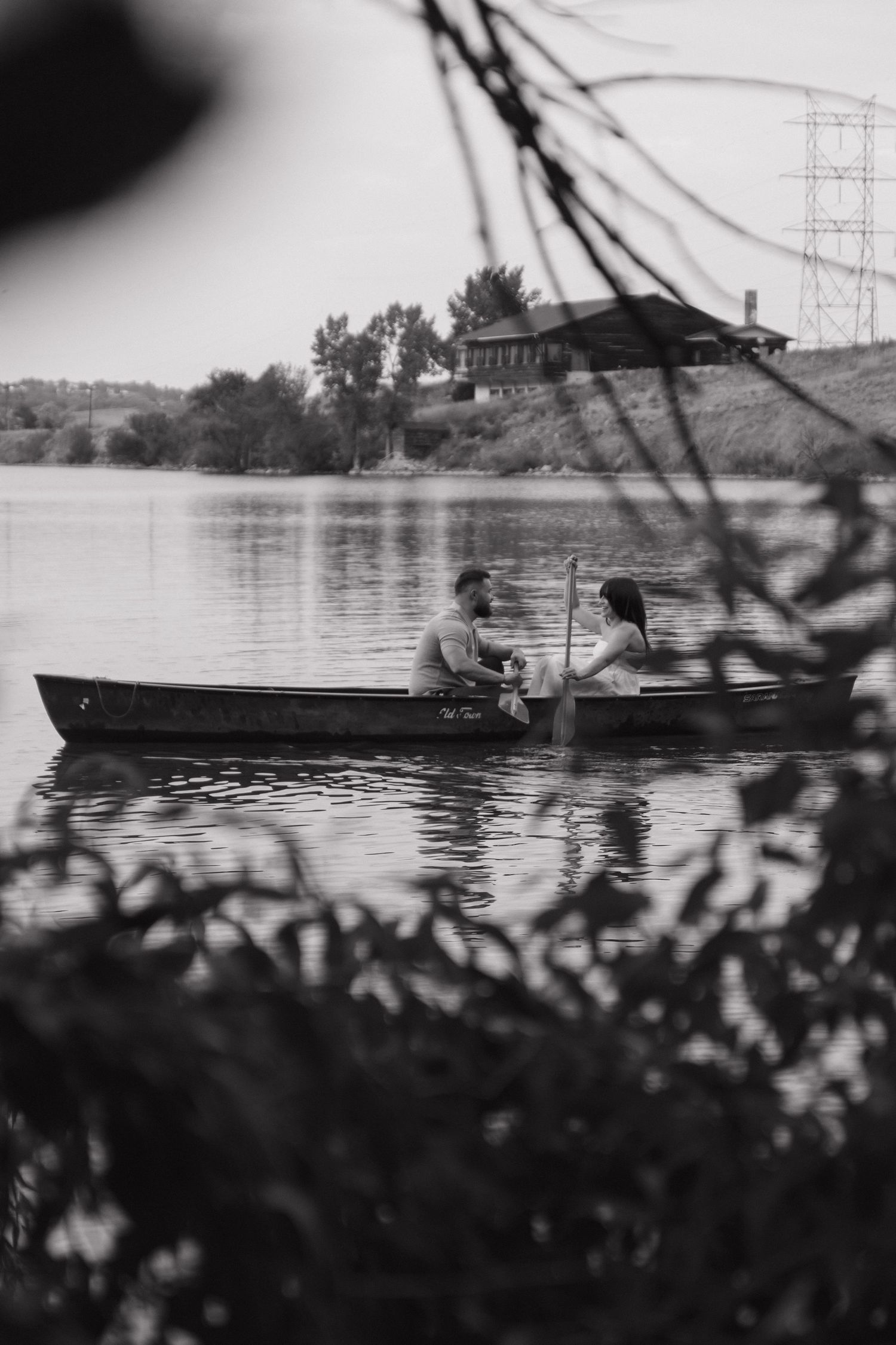 A black and white scenic view of a rowboat drifting on calm lake waters with mountains in the background.