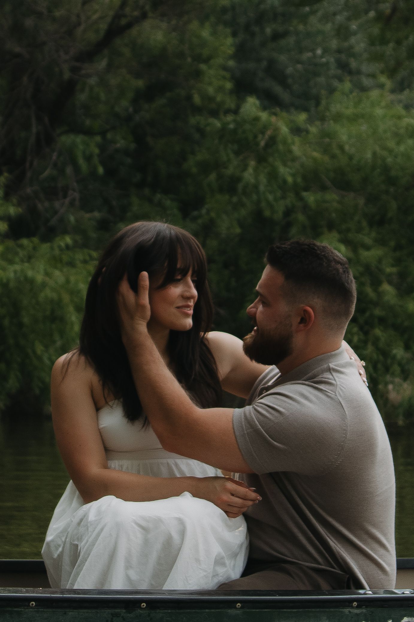 A romantic couple embrace in a series of intimate moments while sitting in a boat on a tranquil lake surrounded by greenery.