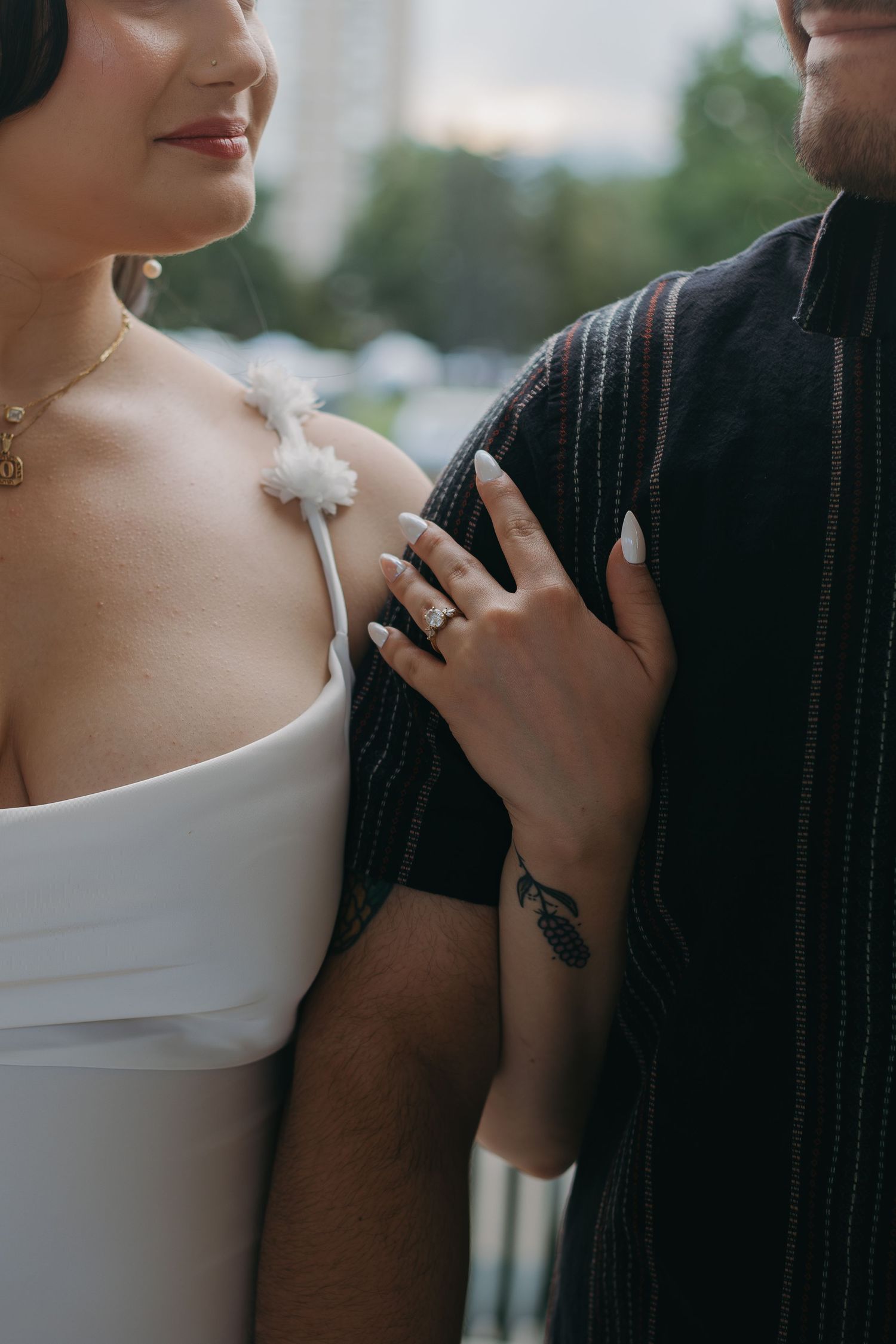 Close-up of a couple in formal attire standing close together, highlighting jewelry and fashion details.