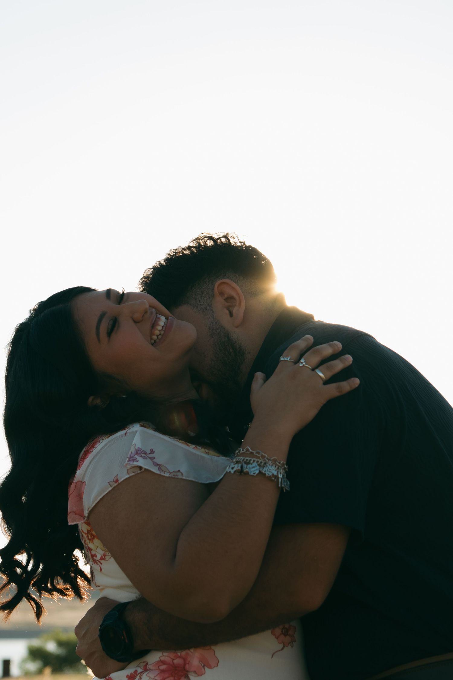 A romantic couple shares a tender embrace during sunset in an outdoor setting.