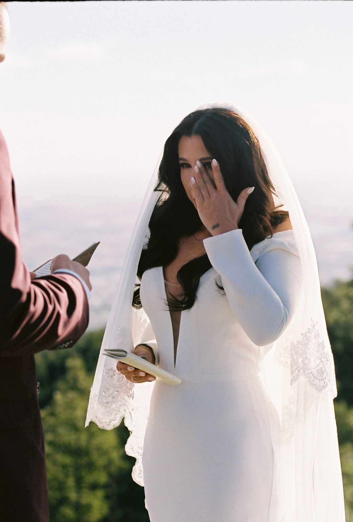 A bride in a white lace wedding dress stands outdoors in a series of candid moments during a photoshoot.
