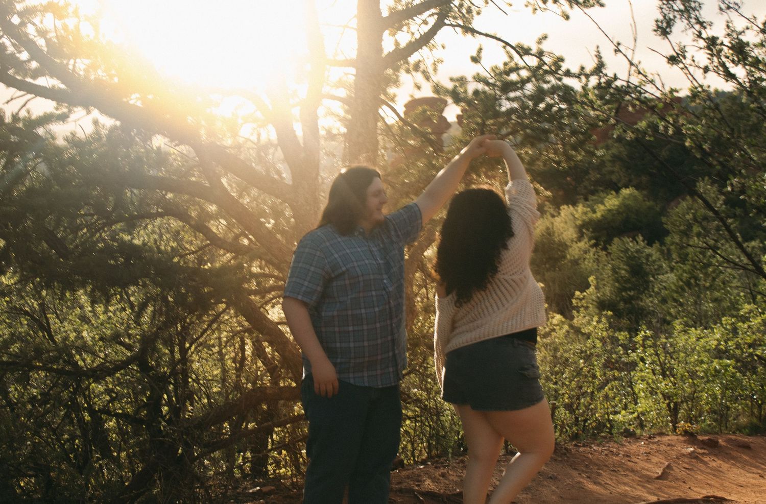 A couple dances together in nature during sunset with sunlight filtering through trees.