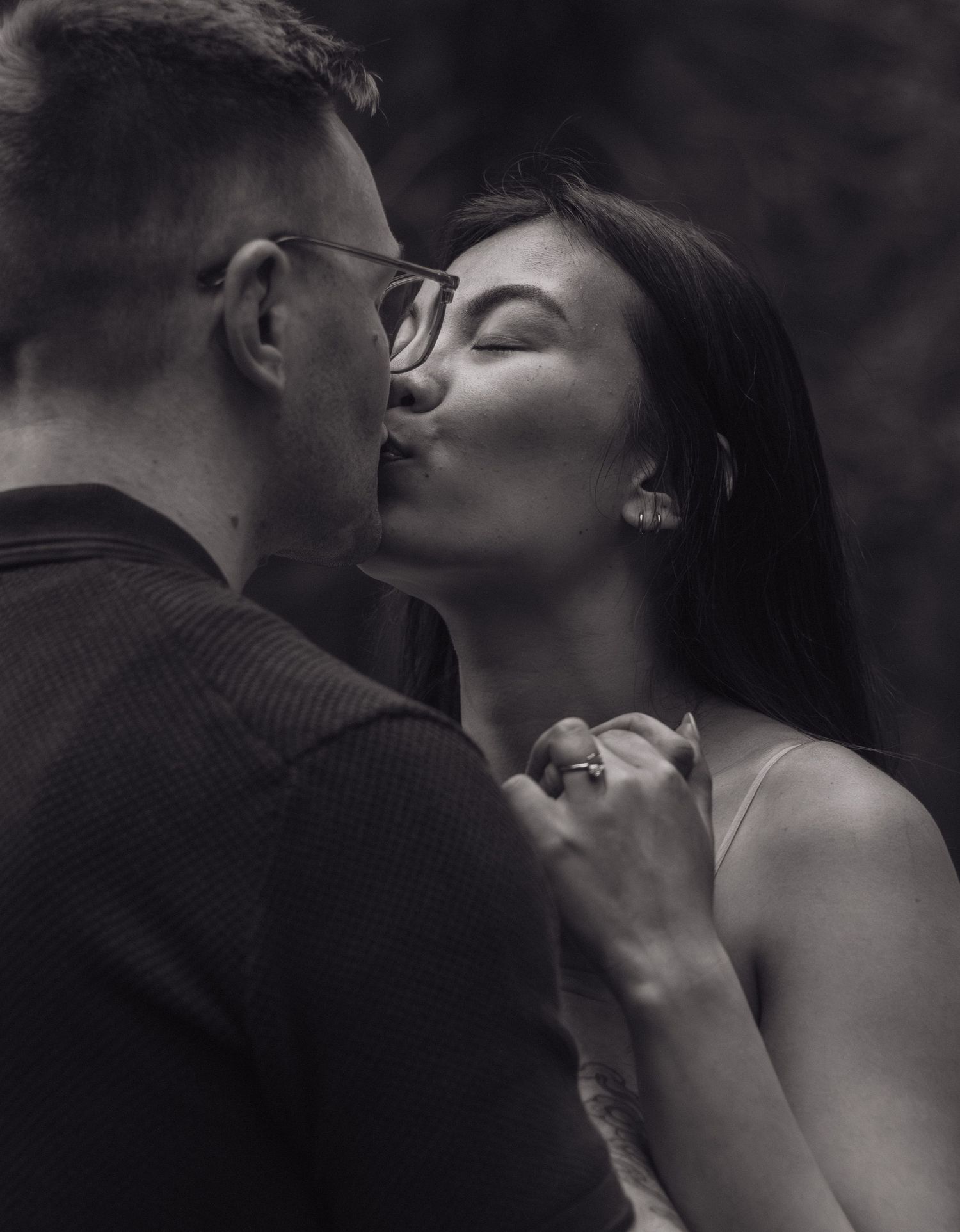 An intimate black and white portrait of a couple sharing a tender kiss outdoors.