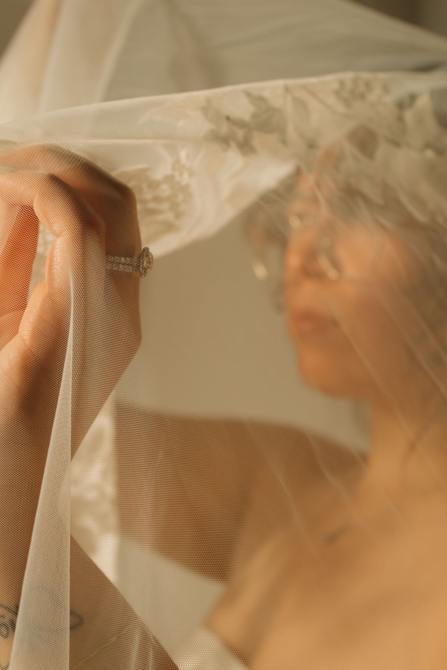 Close-up of a bride's hand holding her veil, with diamond ring visible through sheer fabric.