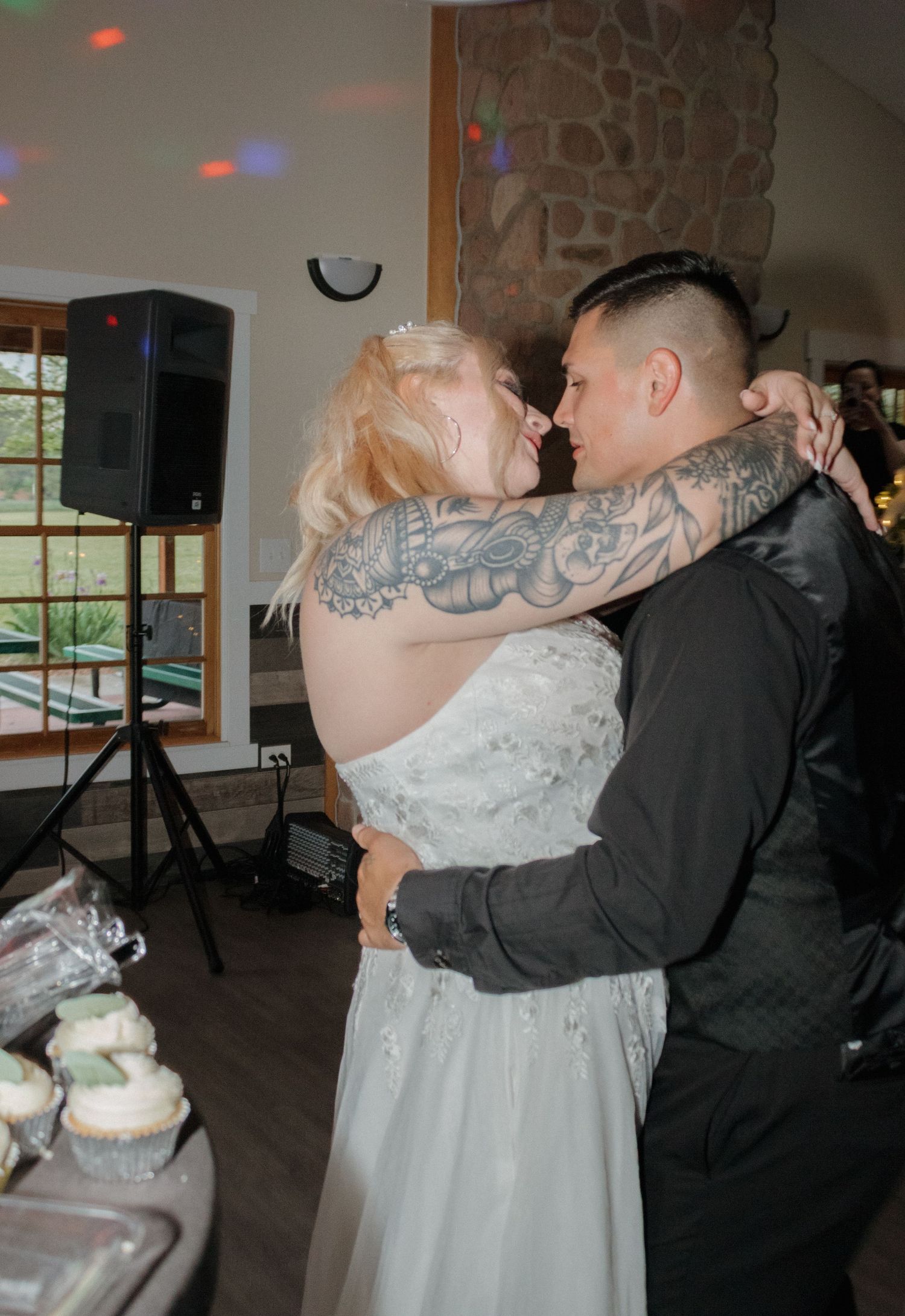 Couple sharing intimate dance moment near cupcake display at wedding reception.