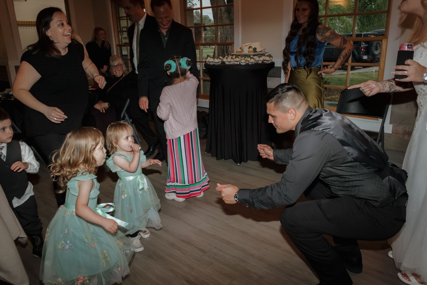 Wedding guests dance and interact with young children in matching mint green dresses on a dance floor.
