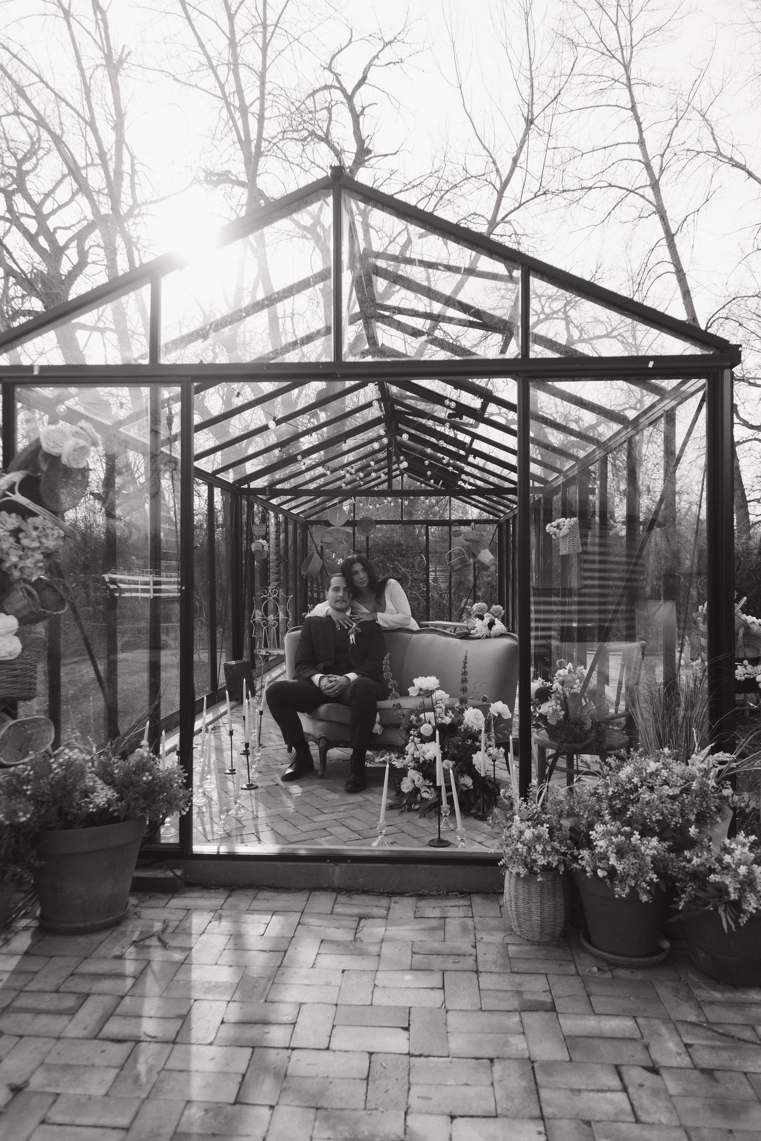 Black and white photo of bride and groom sharing an intimate moment inside a glass greenhouse.