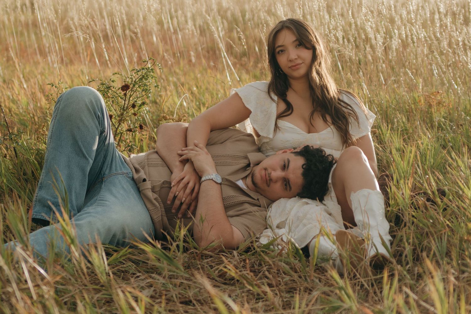 Couple relaxing together in a sunlit golden grass field, woman resting on mans shoulder.