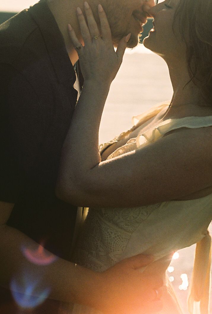 Close-up of couple sharing a passionate kiss bathed in warm golden sunset light outdoors.
