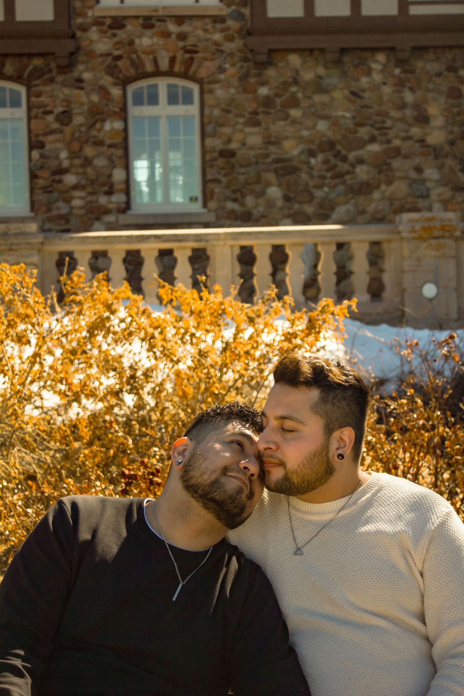 A couple sharing a warm embrace on a bench against stone architecture and fall colors.