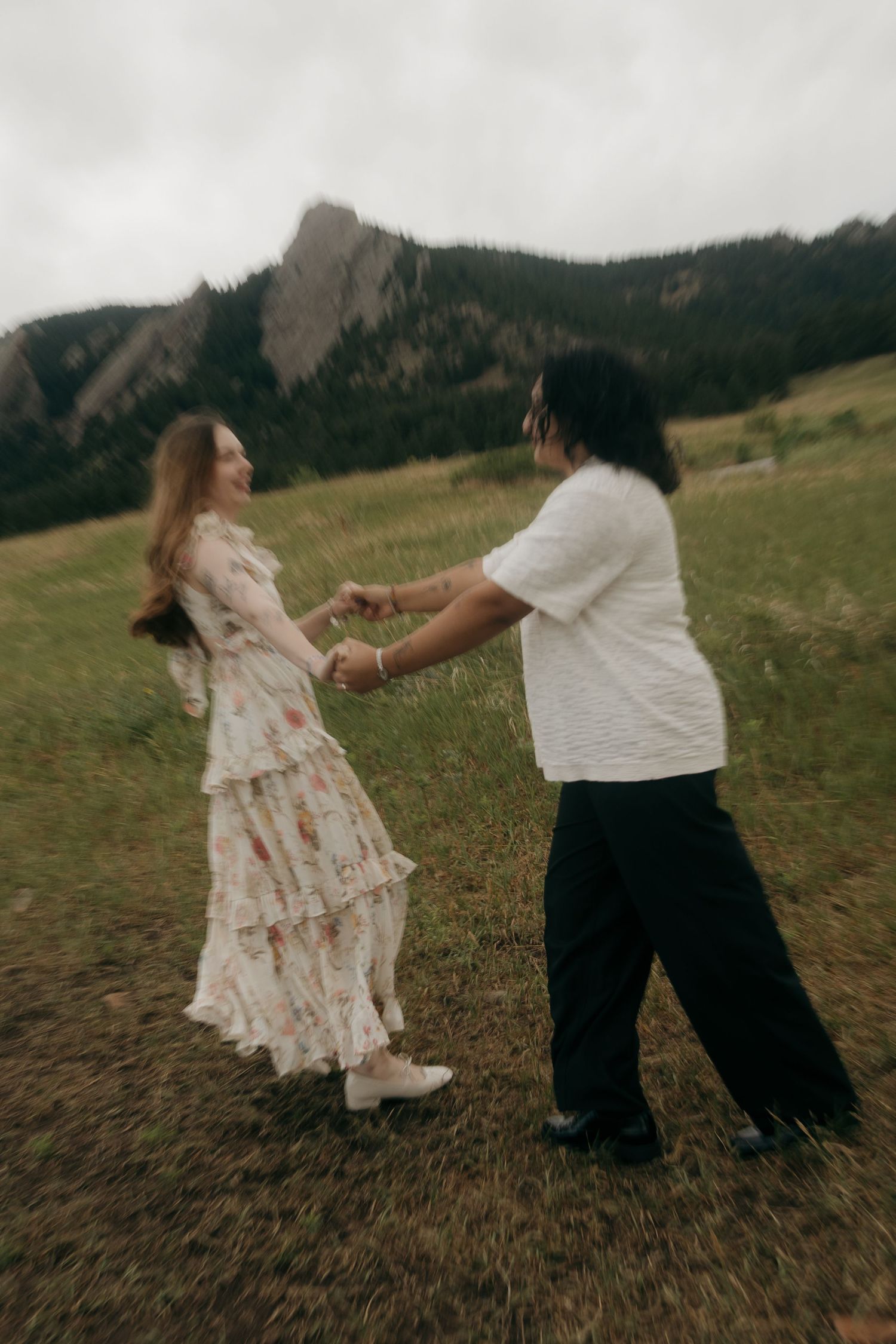 Couple dancing and holding hands in a green meadow with the Flatirons mountains in the background.