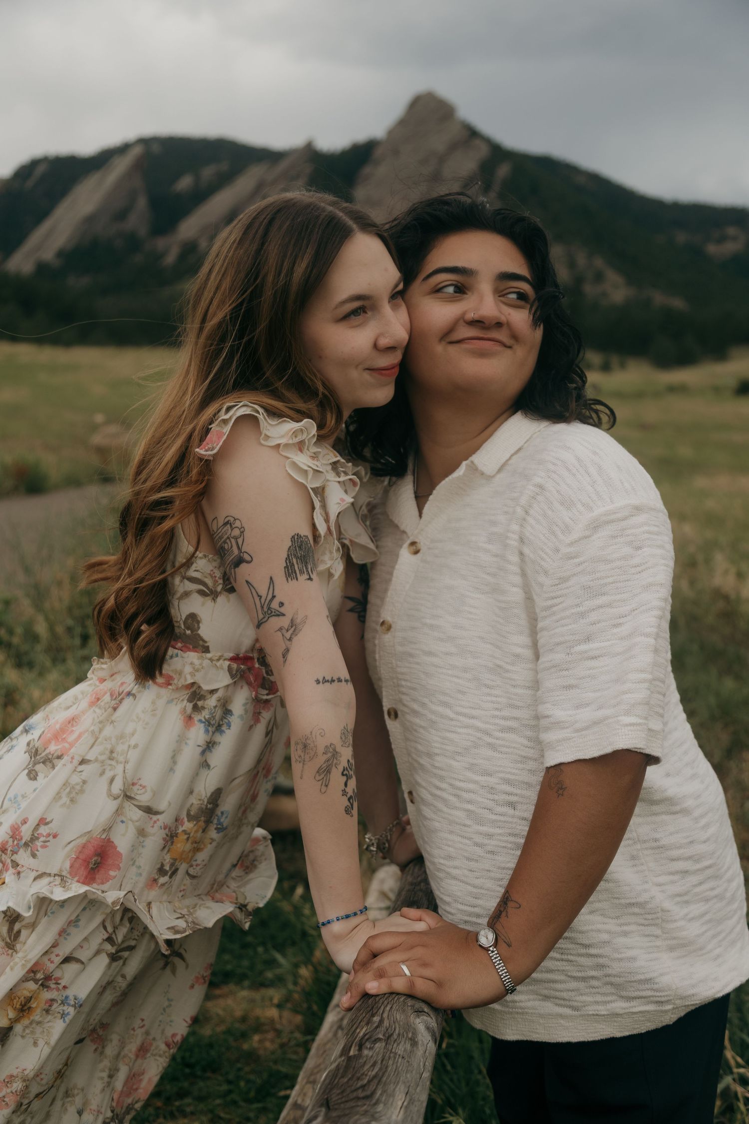 Two women posing together at a wooden fence with the Colorado Flatirons in the background.